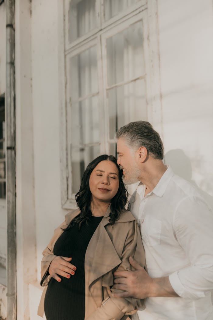 Expectant couple sharing a tender moment by the window in natural light.
